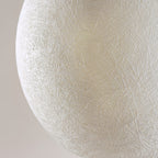 Close view of the fine, interwoven fibre threads on the white shell of this Clérachic pendant, soft grey behind.