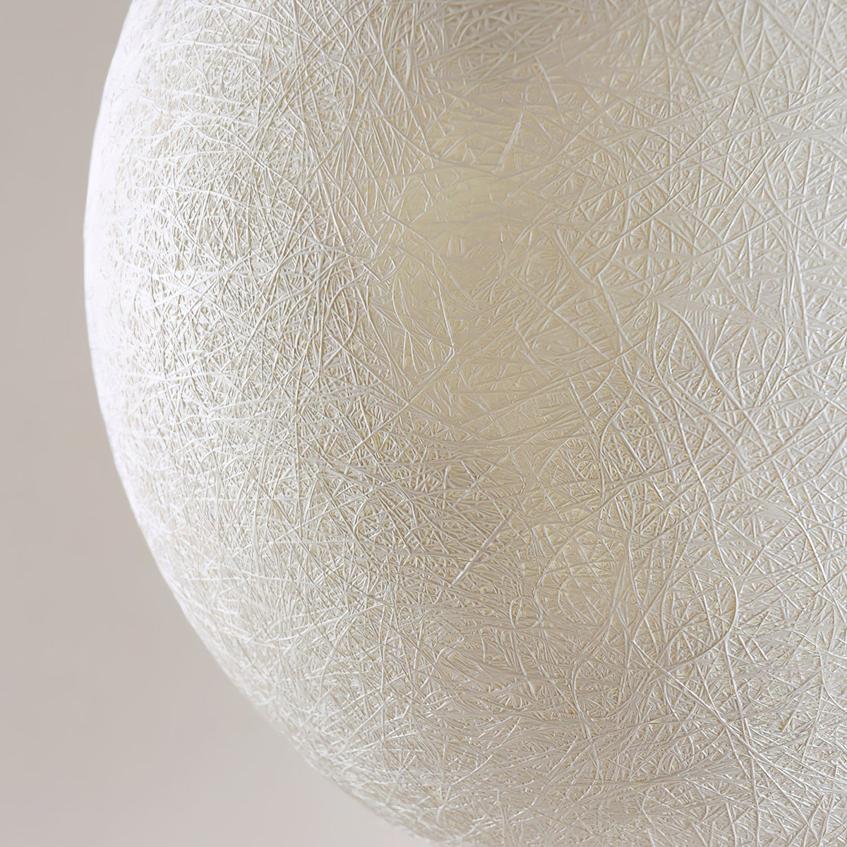 Close view of the fine, interwoven fibre threads on the white shell of this Clérachic pendant, soft grey behind.