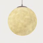Lit Clérachic sphere glowing warm yellow, its crater-like surface visible, hung from a grey canopy against a pale backdrop.