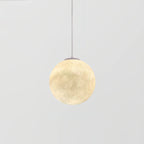 The smallest Clérachic sphere pendant, lit warm cream on a thin cord, against a light grey backdrop.