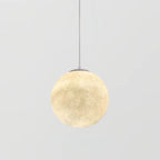 Compact lit Clérachic sphere pendant, textured and cream-coloured, hanging from a thin white cord on light grey.