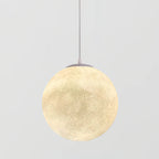 The largest Clérachic sphere pendant, lit warm cream, nearly filling the frame on its thin cord against pale grey.