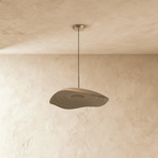 Clérachic wavy, layered resin pendant in taupe, unlit, hanging from a polished metal canopy over a plaster wall