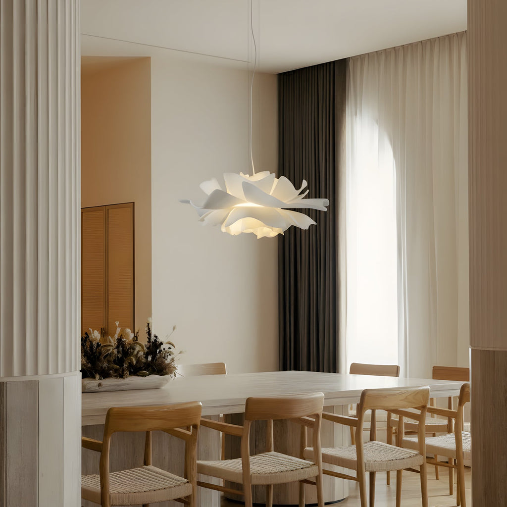 Clérachic white petal pendant glowing softly above a long white dining table with light wooden chairs and tall linen curtains.