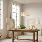 Clérachic white petal pendant in a bright studio with a rustic wooden table, painted canvases and a leafy plant.