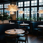 Clérachic white petal pendants glowing in a dark restaurant with big black-framed windows and round marble tables.