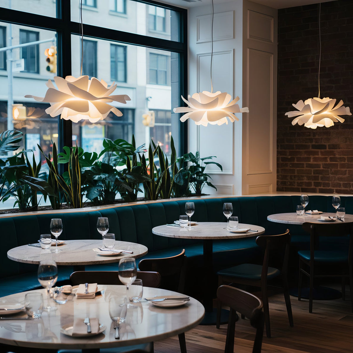 Clérachic white petal pendants hung at different heights in a restaurant, above round tables and a blue-green banquette.