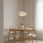 Clérachic white petal pendant above a small round oak table with woven-seat chairs, against a pale wall and a long curtain.