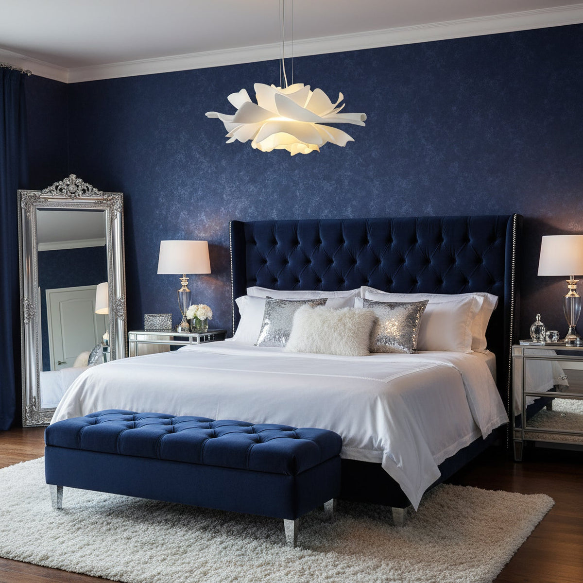 Clérachic white petal pendant above a bed with a navy tufted headboard, a navy bench and a tall silver-framed mirror.