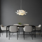 Clérachic white petal pendant against a dark grey wall, above a black dining table with grey chairs.