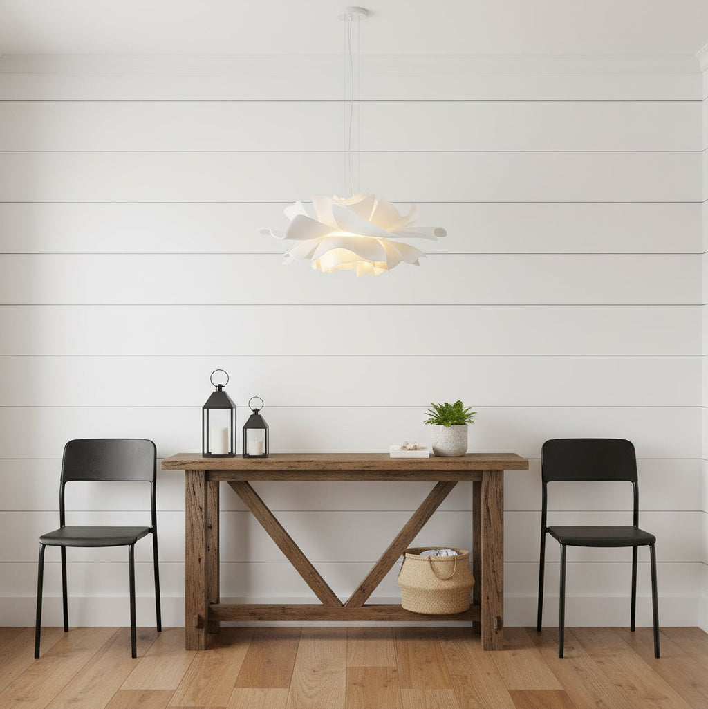 Clérachic white petal pendant against white wall boards, above a rustic console table with two black chairs and lanterns.