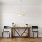 Clérachic white petal pendant against white wall boards, above a rustic console table with two black chairs and lanterns.