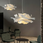 Two Clérachic white petal pendants in a grey lounge, the nearer one large, above chairs and a round black table.