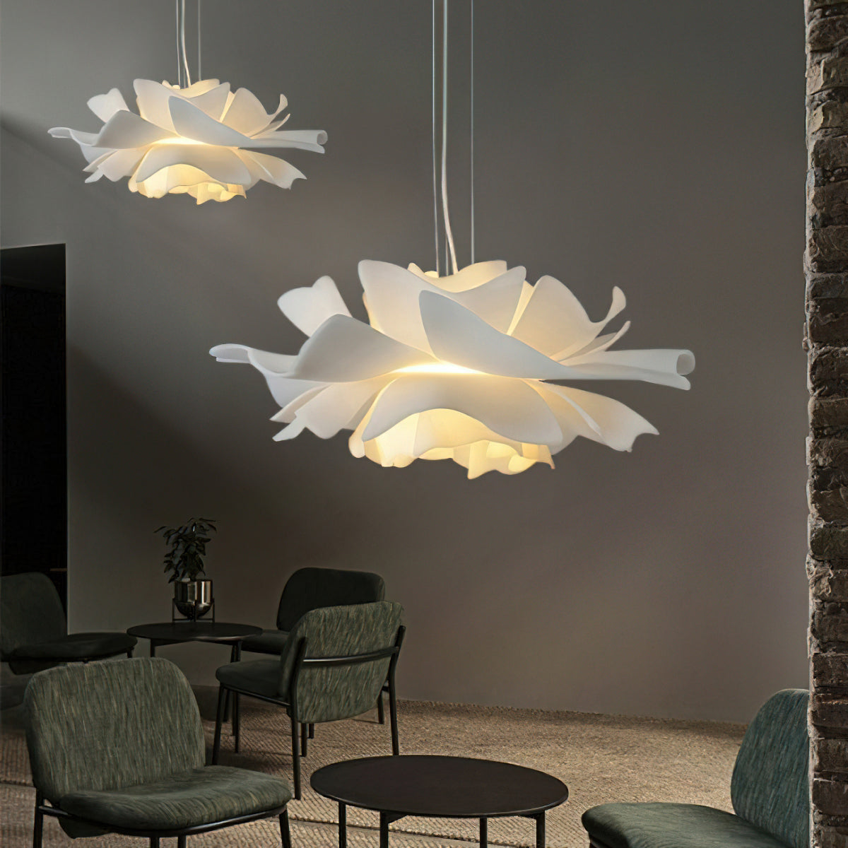 Two Clérachic white petal pendants in a grey lounge, the nearer one large, above chairs and a round black table.