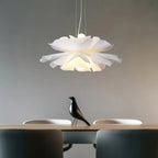 Clérachic white petal pendant with layered ruffled petals above a table with a black bird figure, against a grey wall.