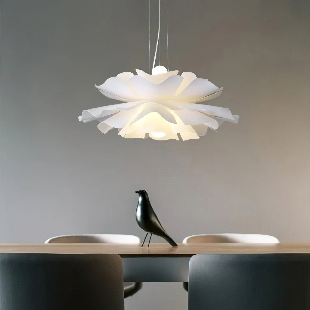 Clérachic white petal pendant with layered ruffled petals above a table with a black bird figure, against a grey wall.