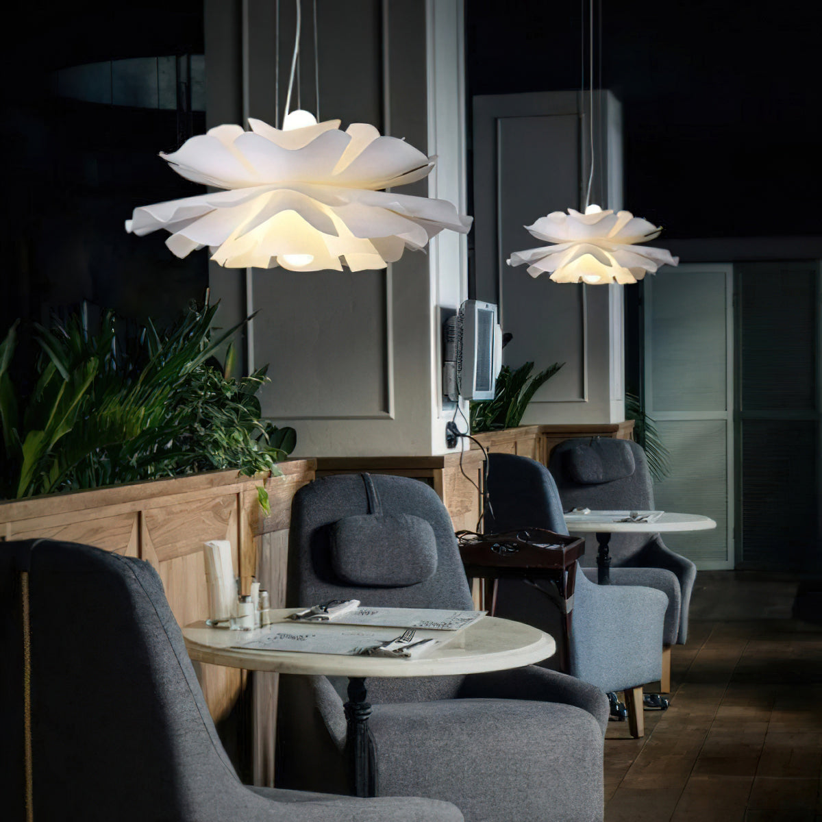 Two Clérachic white petal pendants over a dark restaurant seating area, with grey armchairs and a round table.