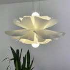 Close view of a Clérachic white petal pendant with its bulb visible above and below the layers, in front of a plant.