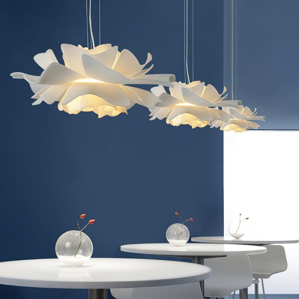 Three Clérachic white petal pendants above round white tables, against a deep blue wall with small glass vases.