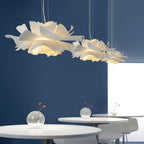 Three Clérachic white petal pendants above round white tables, against a deep blue wall with small glass vases.
