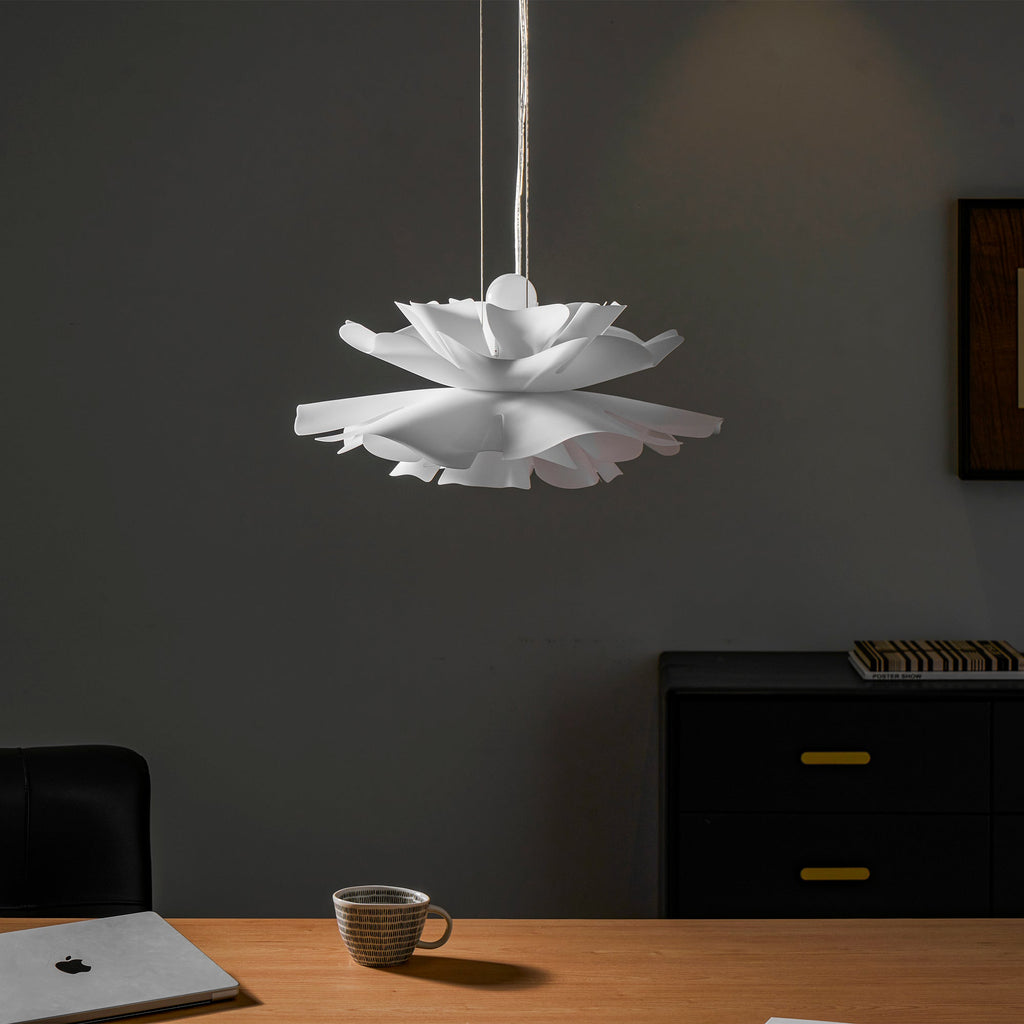 Unlit Clérachic white petal pendant against a dark wall, above a wooden desk with a mug and a laptop.