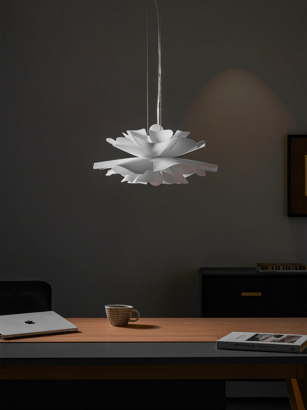 Unlit Clérachic white petal pendant in a dim room, with a desk, a mug, a laptop and a black drawer unit behind it.
