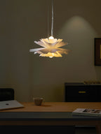Warm light under the layered petals of this Clérachic white pendant, above a desk with a mug and a book.