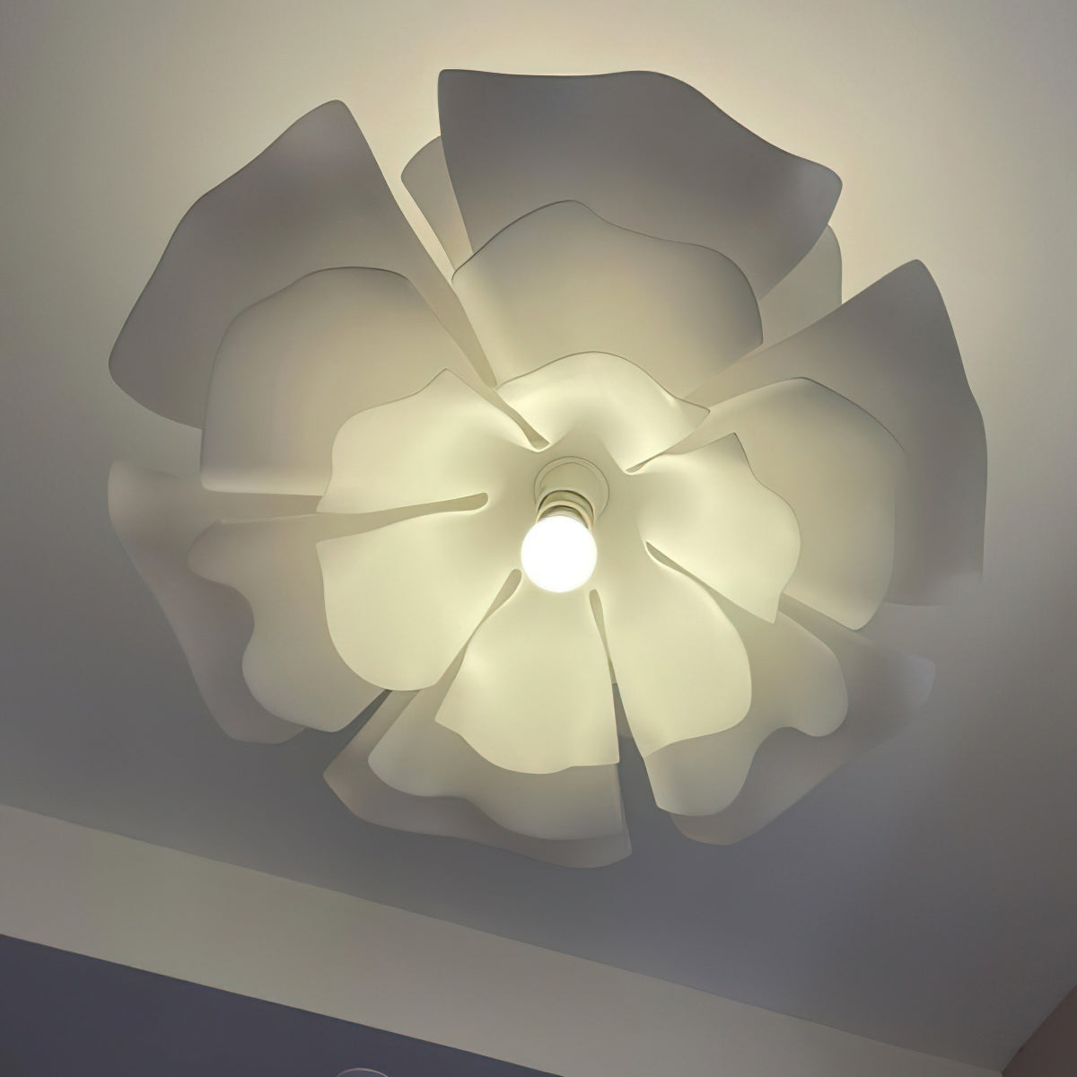 Close view from below of the overlapping petals of this lit Clérachic pendant, with a round bulb at the centre.