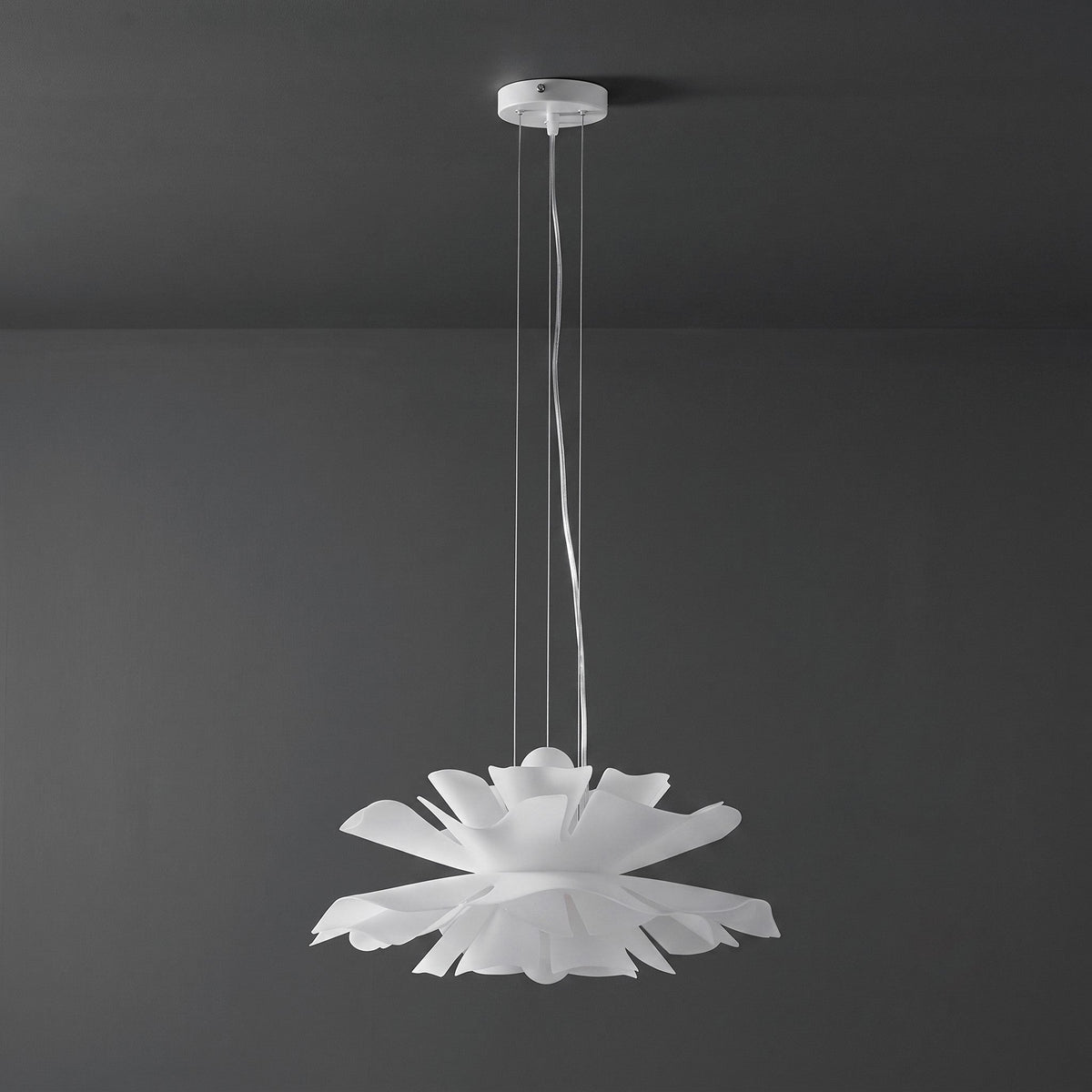 Clérachic white petal pendant with a white ceiling canopy, unlit, against a dark grey wall.