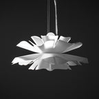 Unlit Clérachic white petal pendant with layered, notched petals, hung on a thin cable against a black backdrop.