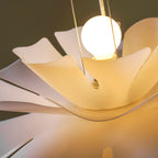 Close view of a warm round bulb glowing inside the upper petals of this Clérachic pendant.