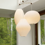 A trio of lit white Clérachic pendants in pear, oval and ball shapes hangs together in front of tall green-framed windows.