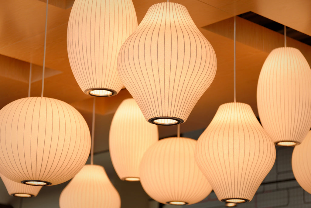 Looking up at a cluster of lit Clérachic pendants, the ribbed white shades glow amber against a warm, golden ceiling.