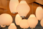 Looking up at a cluster of lit Clérachic pendants, the ribbed white shades glow amber against a warm, golden ceiling.