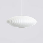 A flat, wide Clérachic pendant in white hangs on grey, with a darker opening visible beneath the ribbed shade.