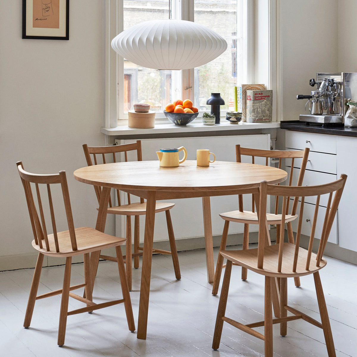 Over a round oak table with four wooden chairs, this wide Clérachic pendant hangs in front of a sunlit kitchen window.