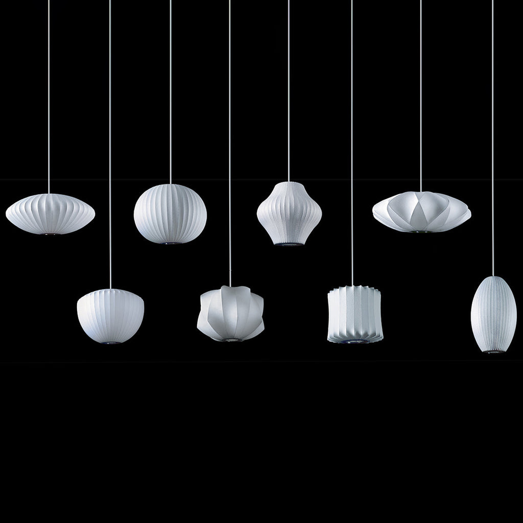 On a black backdrop, eight white Clérachic pendants in different shapes hang at staggered heights, each with a ribbed shade.