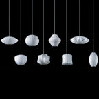 On a black backdrop, eight white Clérachic pendants in different shapes hang at staggered heights, each with a ribbed shade.