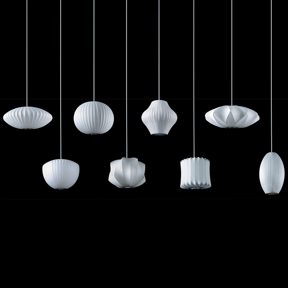 On a black backdrop, eight white Clérachic pendants in different shapes hang at staggered heights, each with a ribbed shade.
