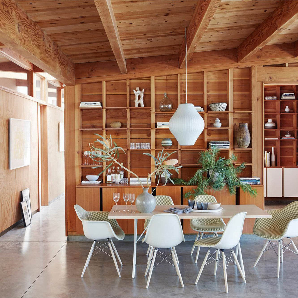 In a timber-lined room, a pear-shaped white Clérachic pendant hangs in front of a tall wooden shelving unit above a white table.