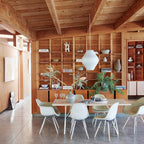 In a timber-lined room, a pear-shaped white Clérachic pendant hangs in front of a tall wooden shelving unit above a white table.