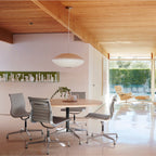 A wide white Clérachic pendant hangs in a room with a pale timber ceiling, above a round table and metal office chairs.