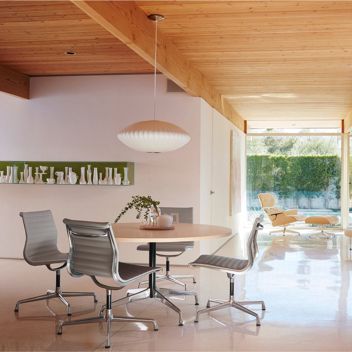 A wide white Clérachic pendant hangs in a room with a pale timber ceiling, above a round table and metal office chairs.