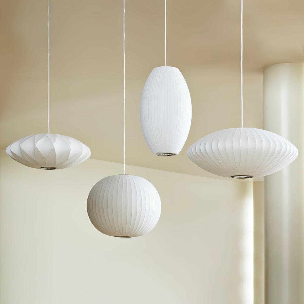 Three Clérachic pendants with ribbed white shades hang at different heights against a warm cream wall, one round, one oval and one wide.