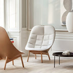 A tall white Clérachic pendant appears at the edge of a pale panelled room with a cream armchair and a low black table.