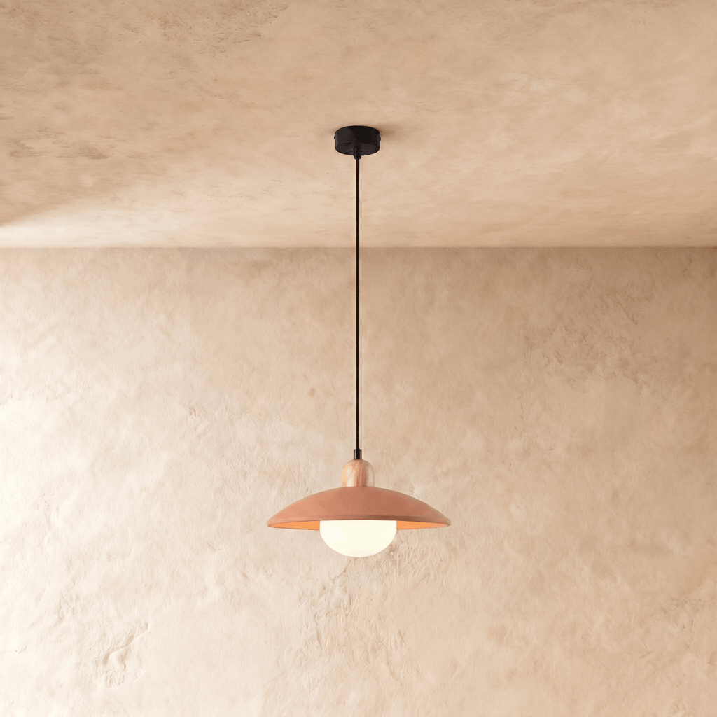 Clérachic pendant light in orange, the saucer shade and opal glass diffuser glowing below a plaster ceiling.