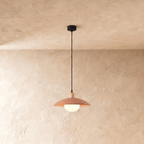 Clérachic pendant light in orange, the saucer shade and opal glass diffuser glowing below a plaster ceiling.