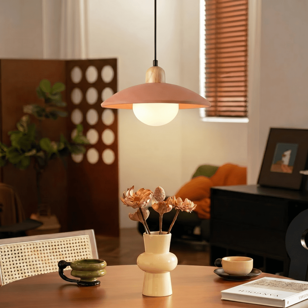 Clérachic orange pendant light glowing above a round table with a ceramic vase, beside a perforated wood screen.