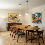 Clérachic white pendant lights, a pair, glowing above a walnut dining table flanked by colourful abstract paintings.