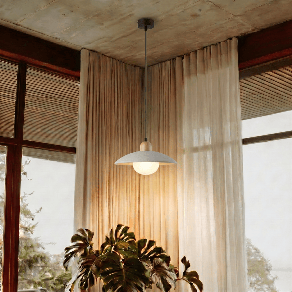 Clérachic white pendant light glowing beside sheer curtains and a large monstera plant near a corner window.